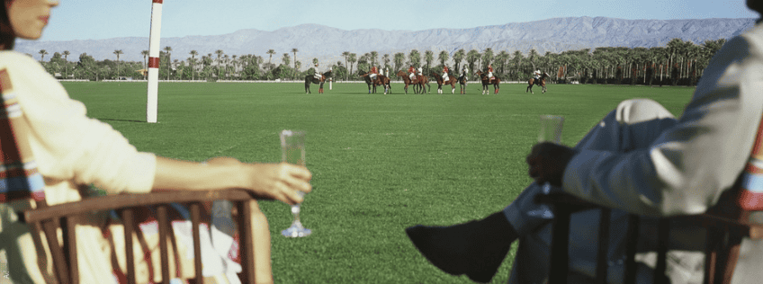 man and woman holding champagne and watching a polo match