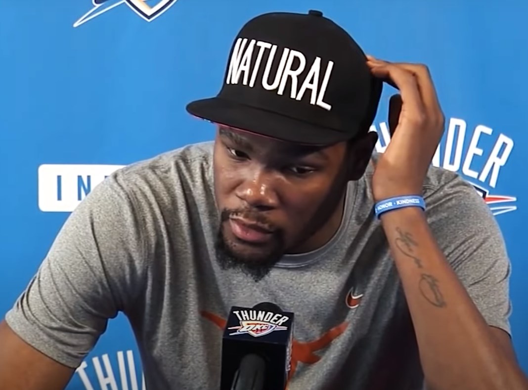 Kevin Durant thinking about something and scratching his head in a black cap