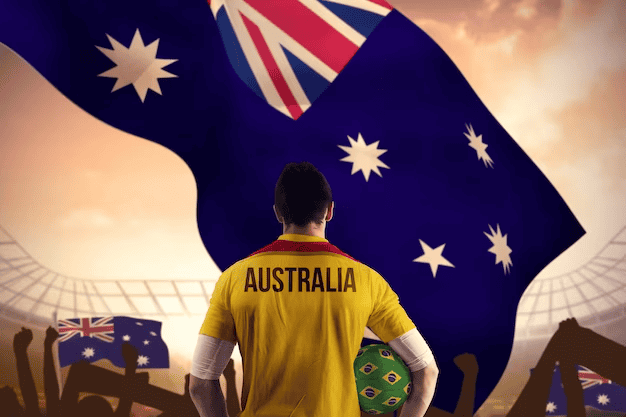 Australian football player holding ball against large football stadium