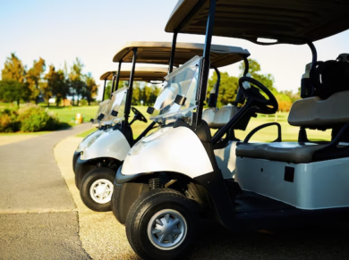 Three golf carts standing side by side next to a golf course