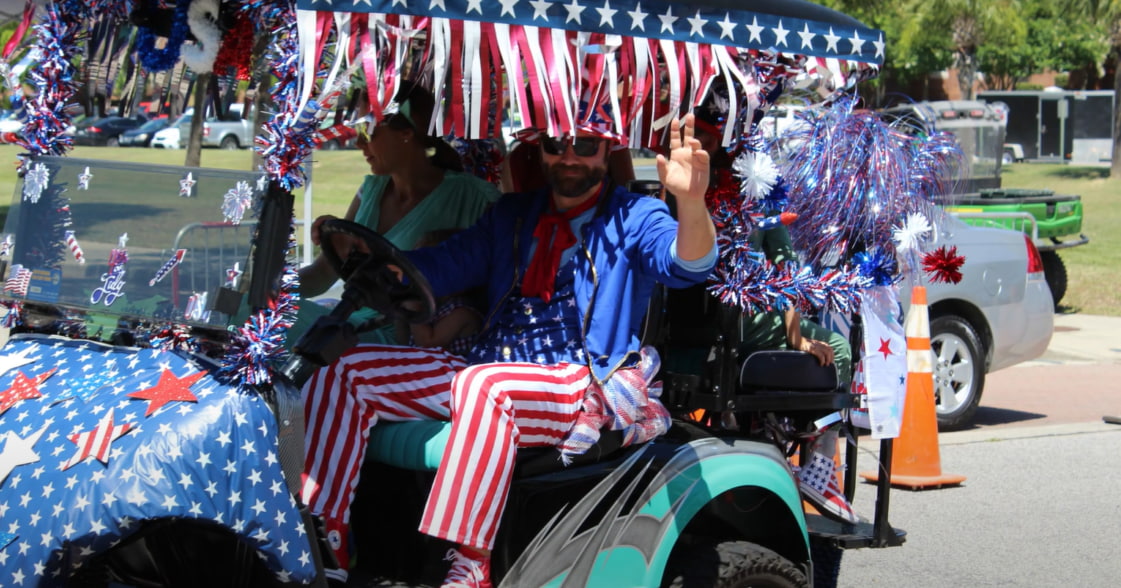 A man sits in a decorated golf cart and waves